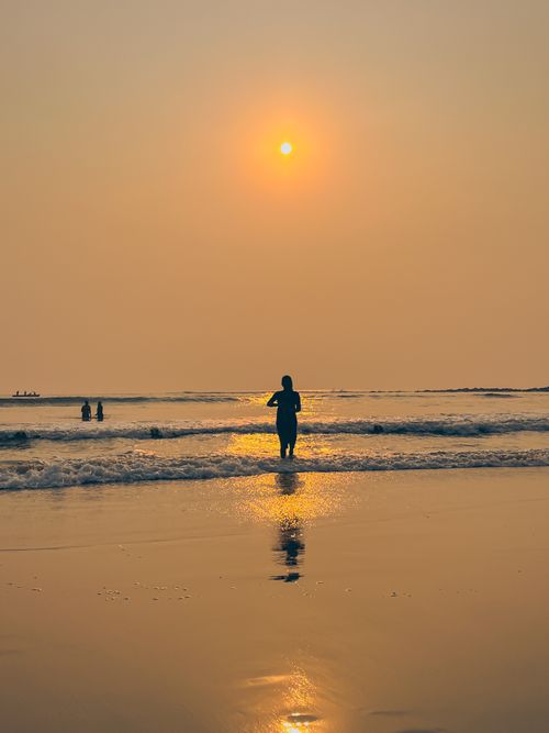 Free A serene sunset on Visakhapatnam beach with a woman standing in the gentle waves, reflecting peace and tranquility. Stock Photo