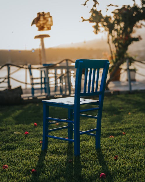 A blue chair sitting on the grass in front of a lake