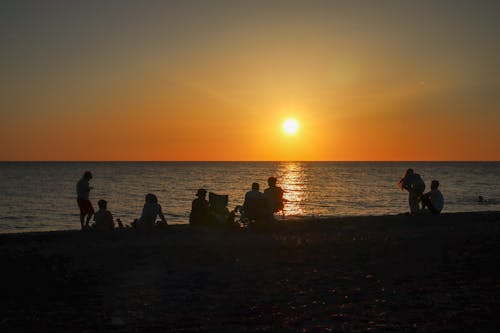 A group of people sitting on the beach at sunset
