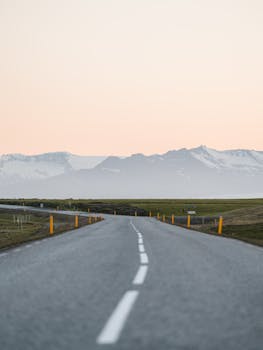 A stunning view of an empty Icelandic road leading towards majestic mountains at sunset, perfect for travel and adventure themes.