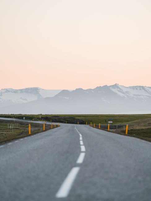 A stunning view of an empty Icelandic road leading towards majestic mountains at sunset, perfect for travel and adventure themes.
