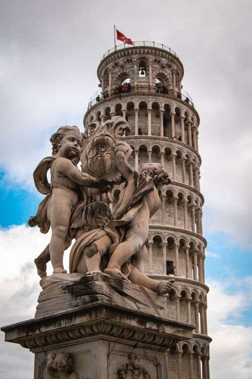 Free A detailed view of a statue in front of the Leaning Tower of Pisa with a cloudy sky backdrop, highlighting Italian architecture. Stock Photo