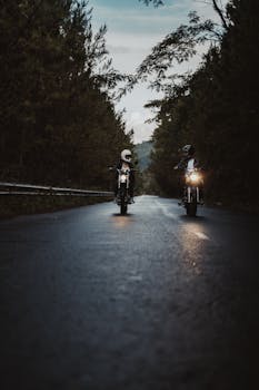 Two motorcyclists ride through a scenic forest road at twilight, capturing an adventurous spirit.