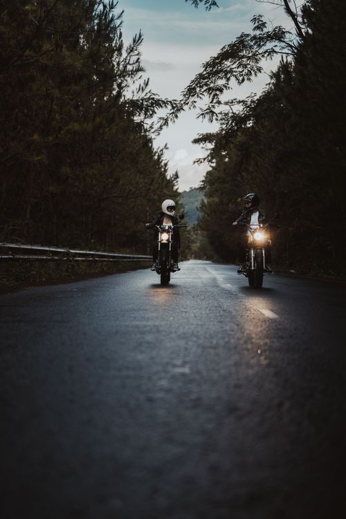 Free Two motorcyclists ride through a scenic forest road at twilight, capturing an adventurous spirit. Stock Photo