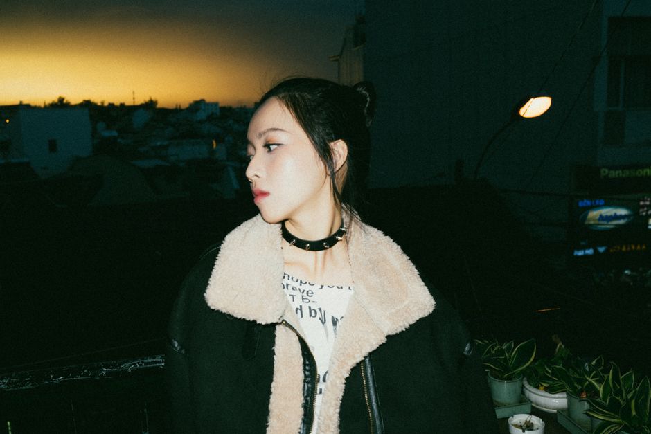 A fashionable woman poses in a leather jacket against a twilight city backdrop.