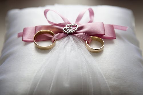 银质订婚戒指套装（带粉红色蝴蝶结装饰）在枕头上的选择性聚焦摄影