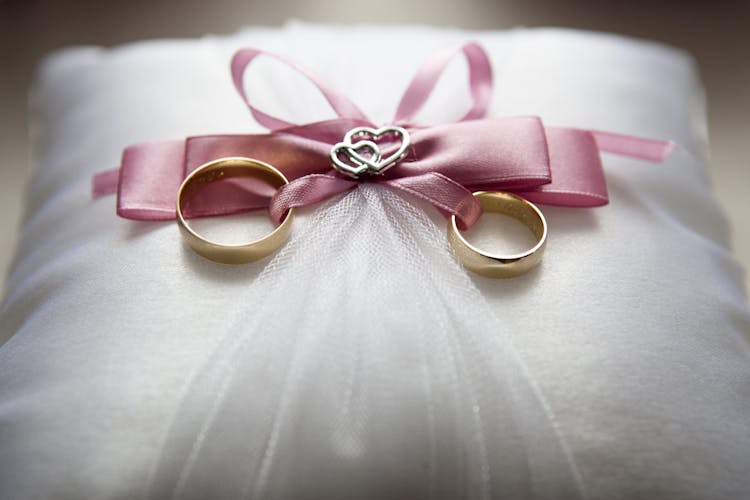 Selective Focus Photography Of Silver-colored Engagement Ring Set With Pink Bow Accent On Throw Pillow