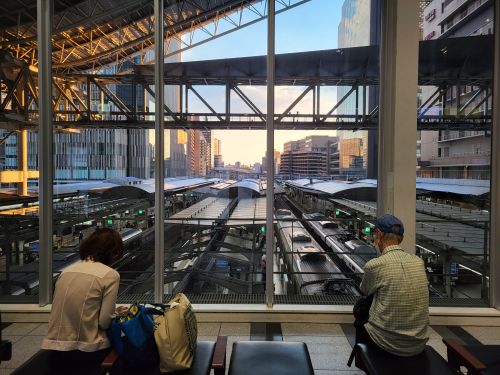 Free A view from inside Osaka Station showing people seated and trains below at sunset. Stock Photo
