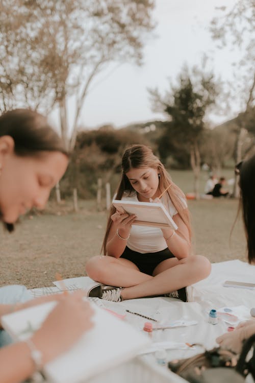 A woman sitting on the grass with two other girls reading