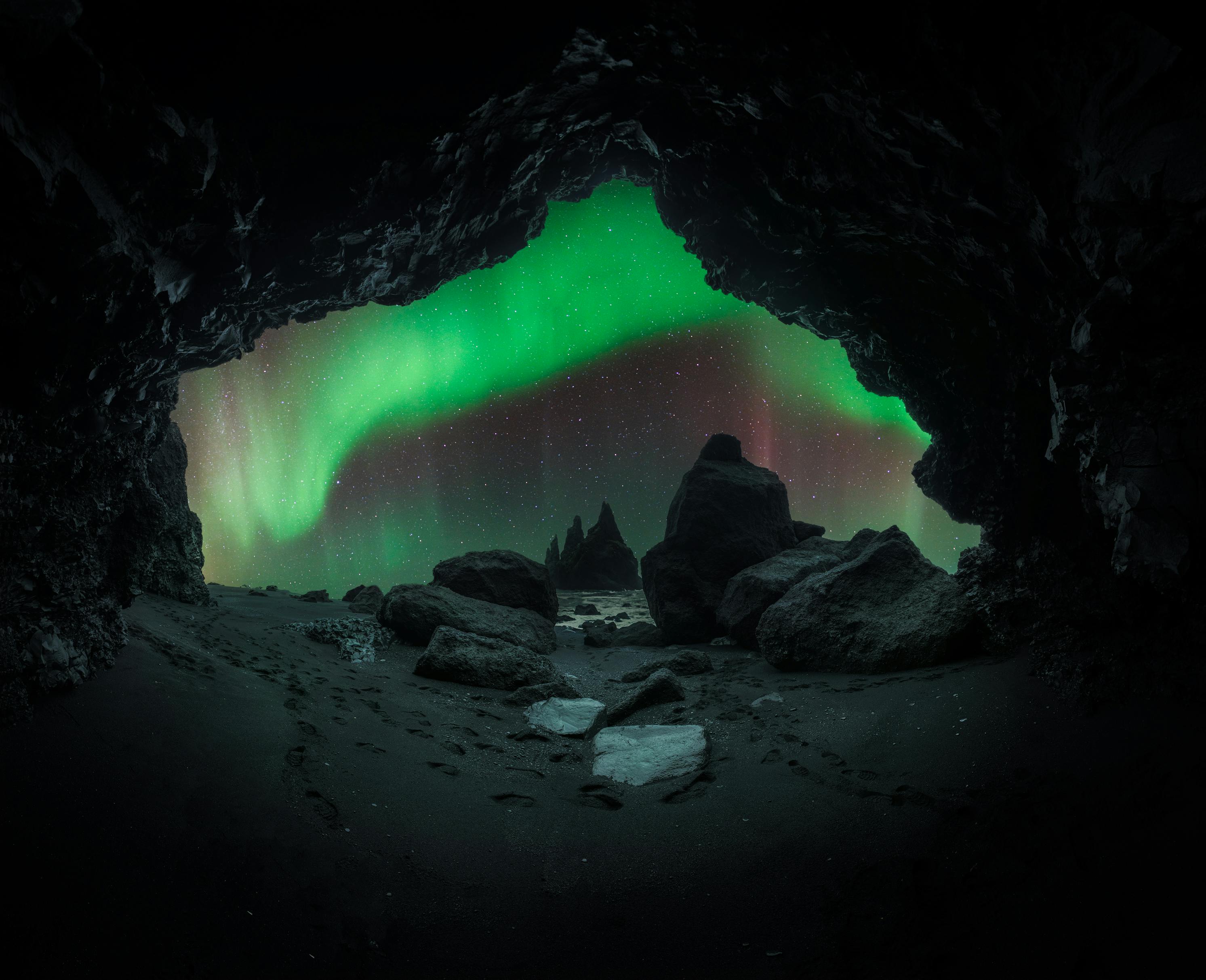 Majestic aurora borealis illuminates the night sky over a rocky cave scene.