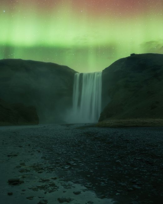 Skogafoss waterfall illuminated by the vibrant aurora borealis in Iceland's scenic landscape.
