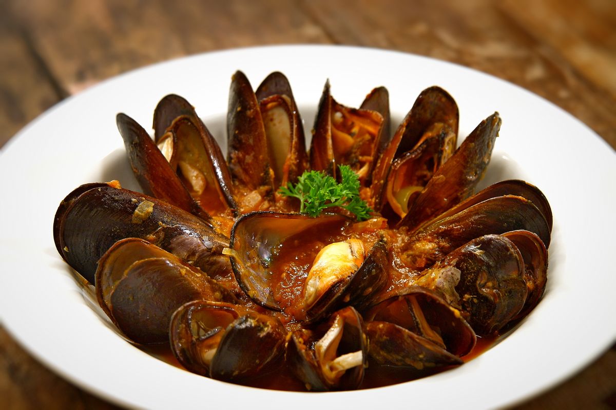 Wide white bowl of opened mussels arranged in a ring in red tomato sauce with parsley