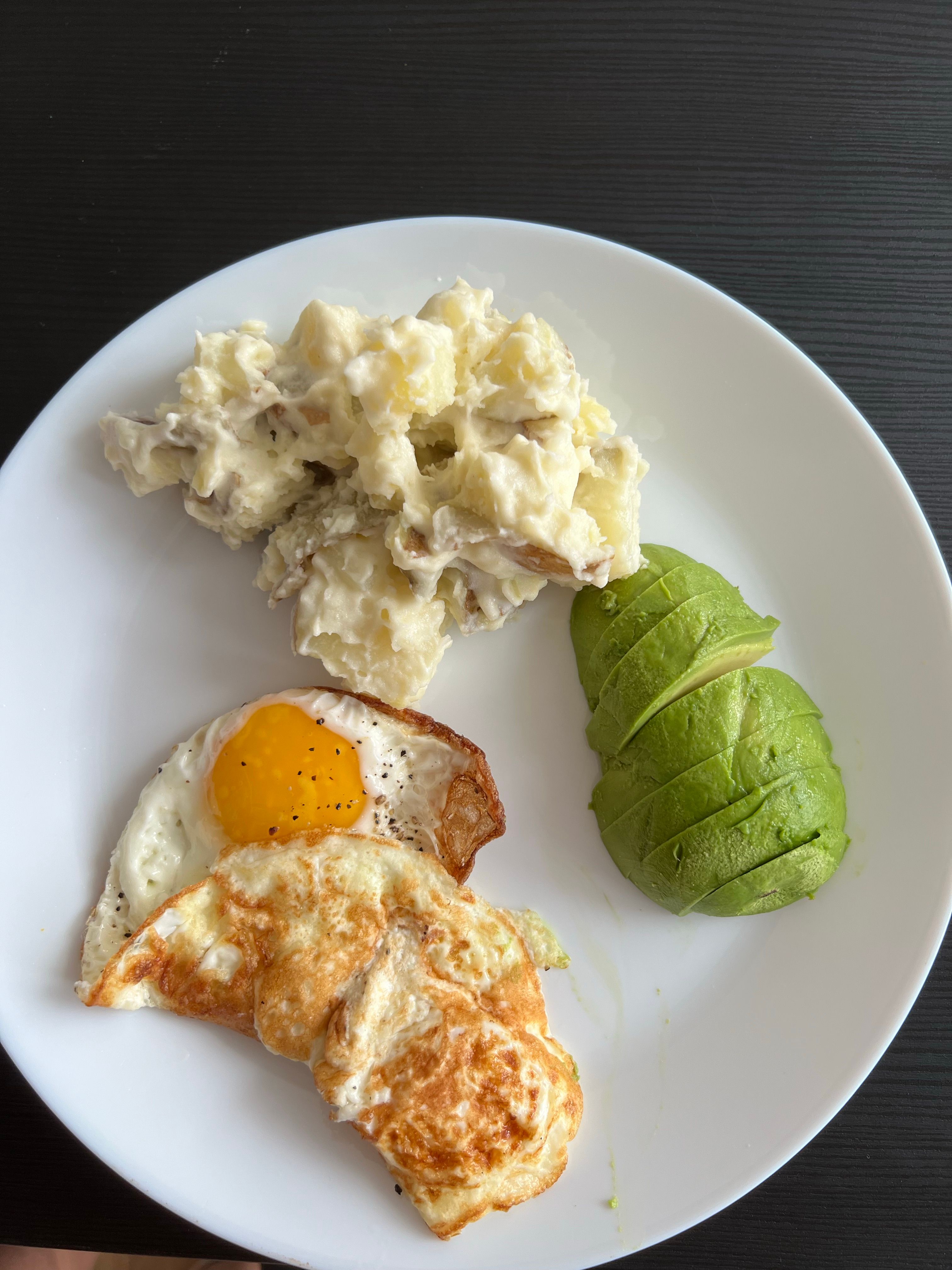 A mouthwatering plate featuring avocado slices, potato salad, and a fried egg.