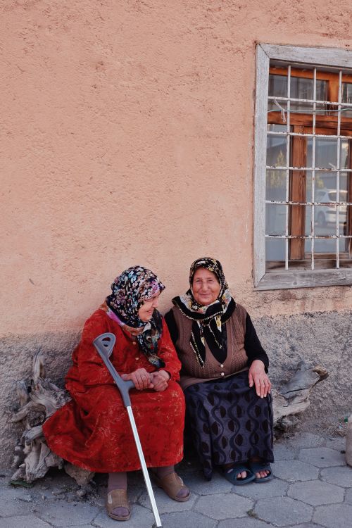 Free Two elderly women in hijabs sit outside a rustic building, sharing smiles and conversation. Stock Photo