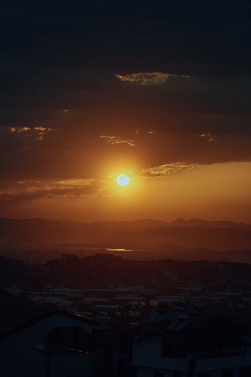 Free A captivating sunset over a city, with mountains silhouetted against a vibrant sky. Stock Photo