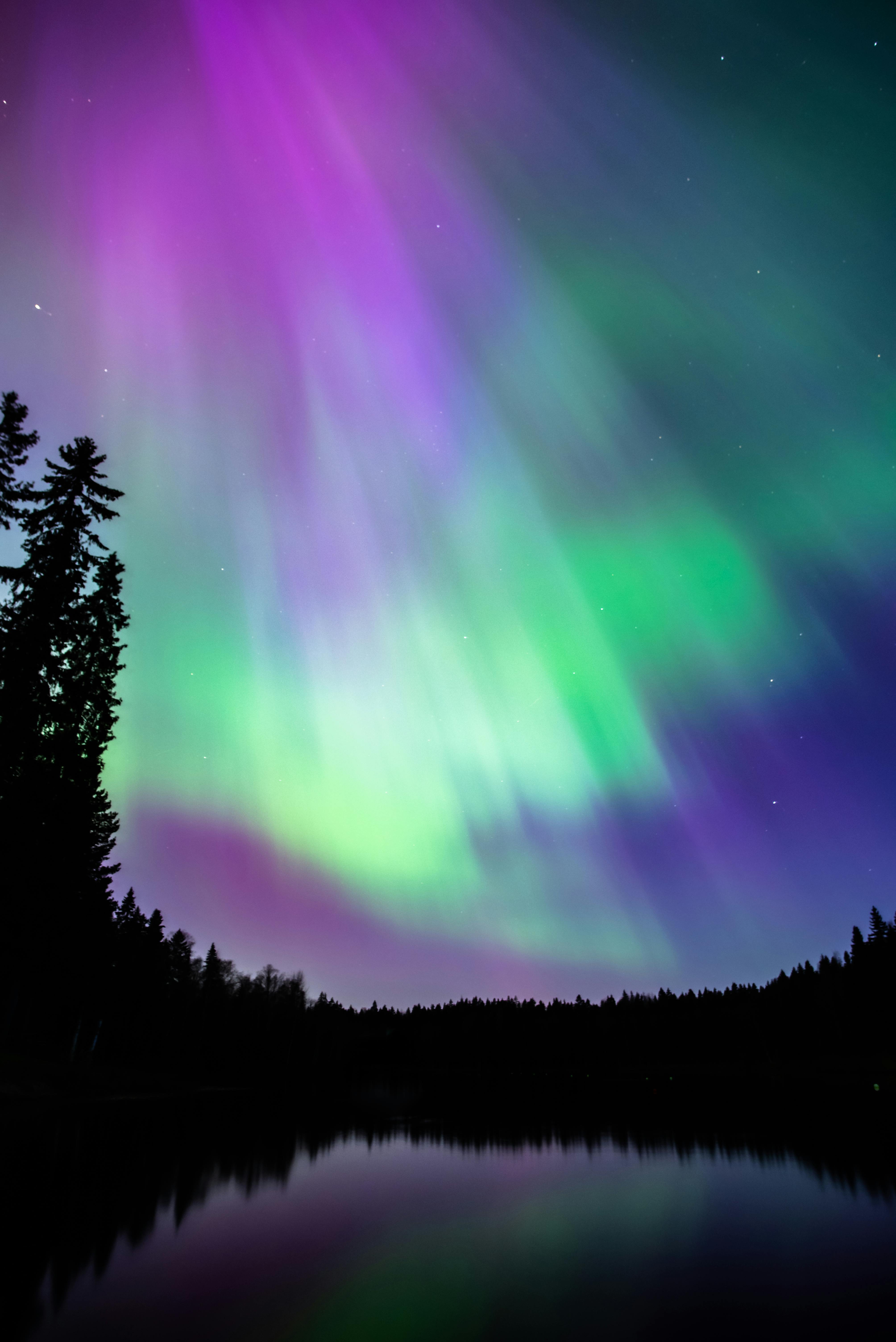 Stunning aurora borealis reflecting over a lake in Tampere, Finland, with vibrant colors lighting the night sky.