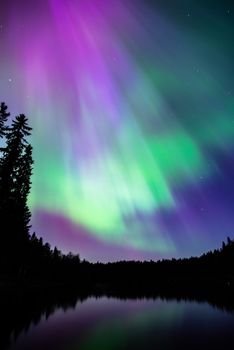 Stunning aurora borealis reflecting over a lake in Tampere, Finland, with vibrant colors lighting the night sky.
