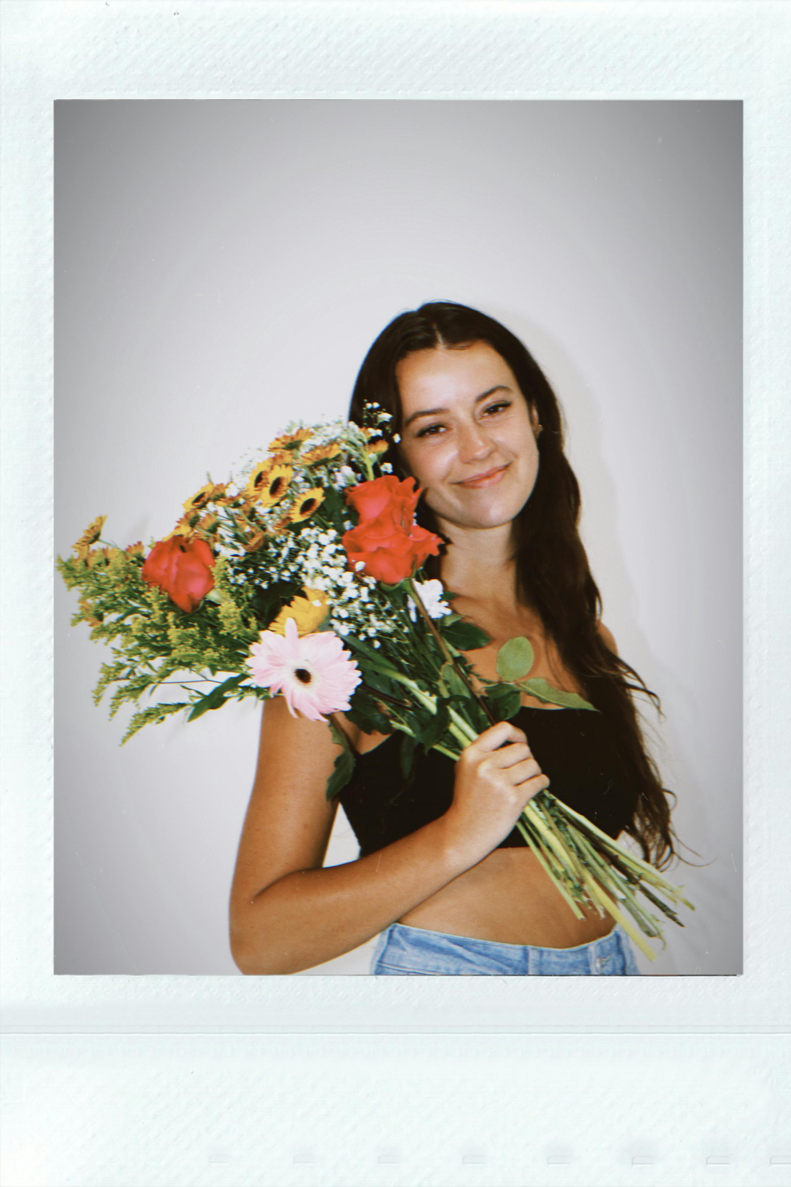 A smiling young woman holds a vibrant floral bouquet, showcasing a floral-themed portrait.