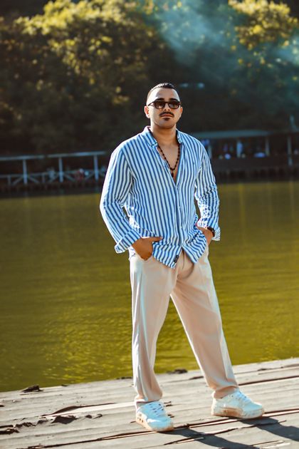 A stylish man in sunglasses and a striped shirt stands by a lakeshore — photo by Murat IŞIK on Pexels