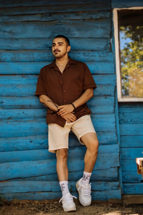 Free Stylish man in a brown shirt stands relaxed against a vibrant blue wooden wall outdoors. Stock Photo