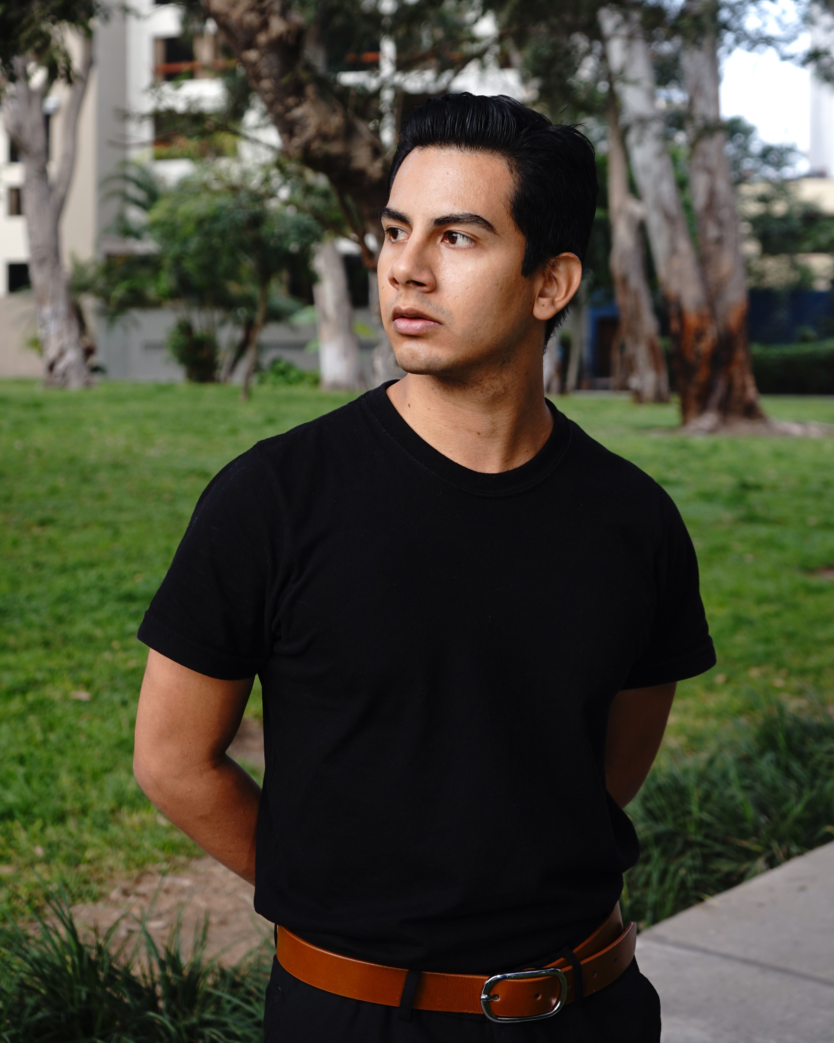 Portrait of a young man in a black t-shirt standing in a park, exuding casual style.