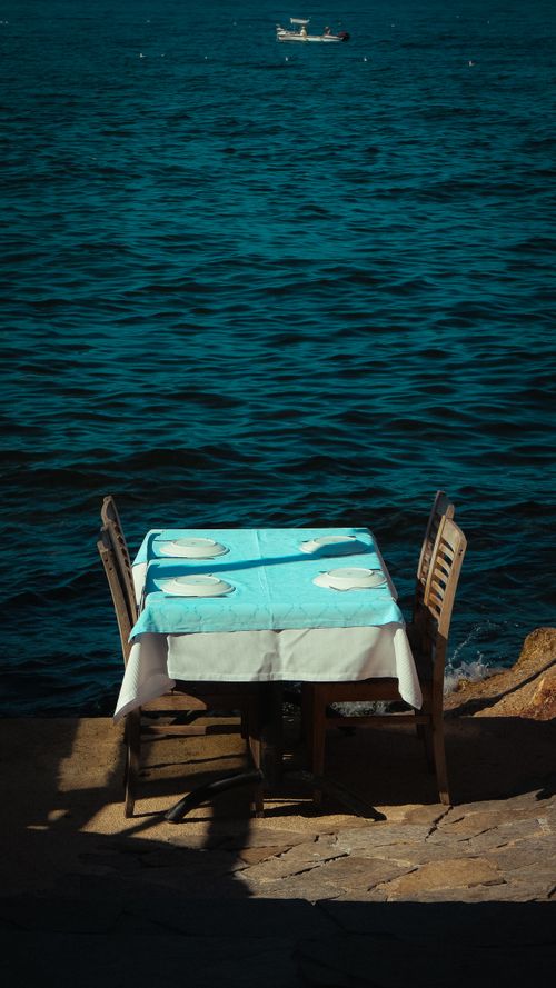 Free Charming oceanfront dining setup with table and chairs by the sea, perfect for a serene meal. Stock Photo