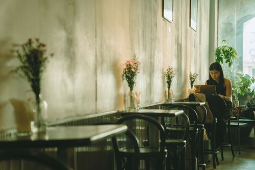 Free A woman working on her laptop in a cozy cafe with elegant floral decor in Ho Chi Minh City. Stock Photo