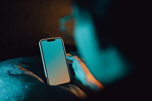 A man holding a smartphone with a blank screen in a dark room, creating a moody ambiance.