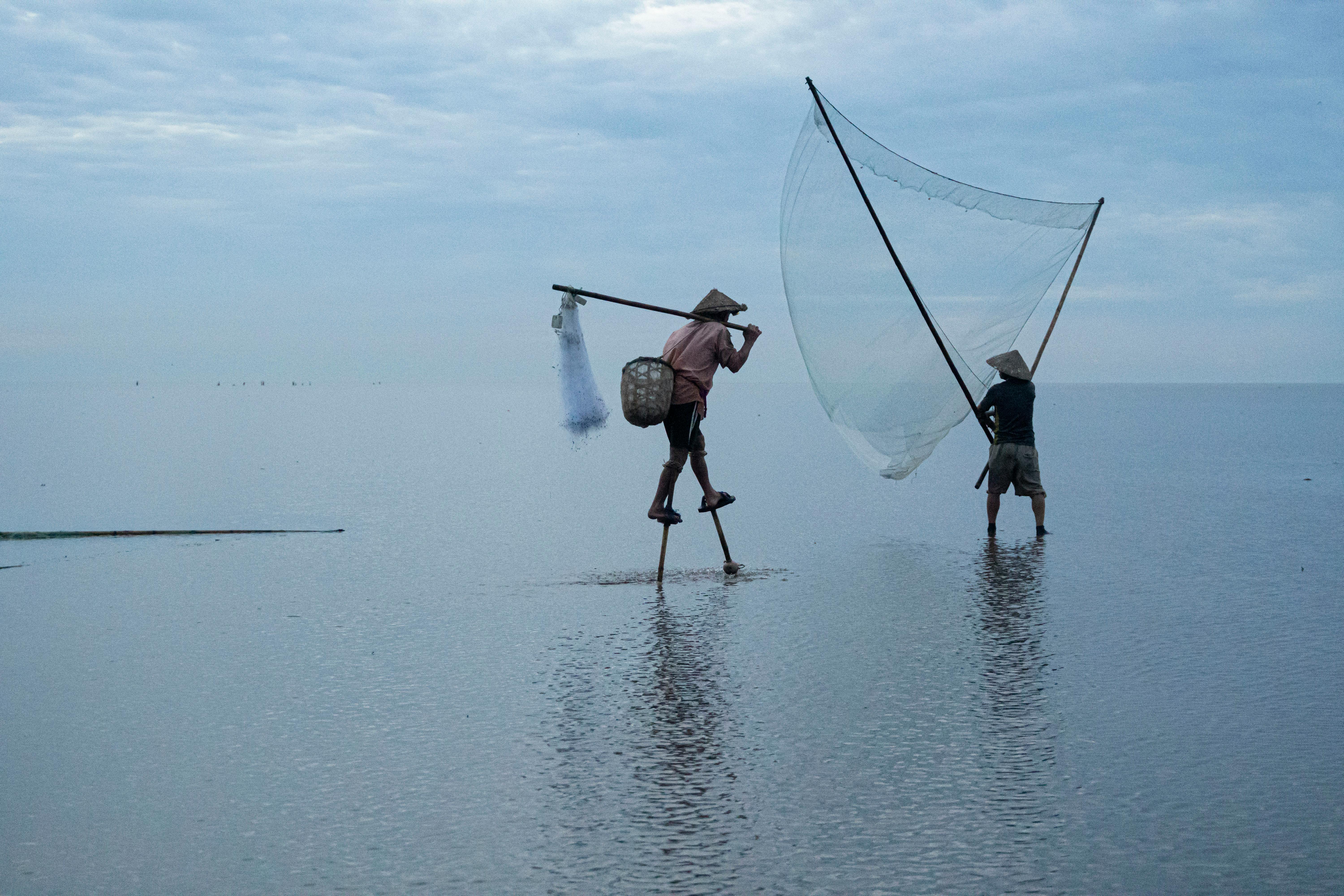 Vietnamese fishermen balancing on stilts with nets in the serene sea at dawn.