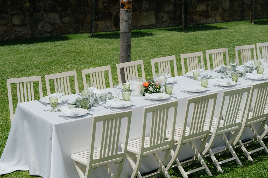 Chic outdoor wedding table with white chairs and floral decor on a sunny summer day.