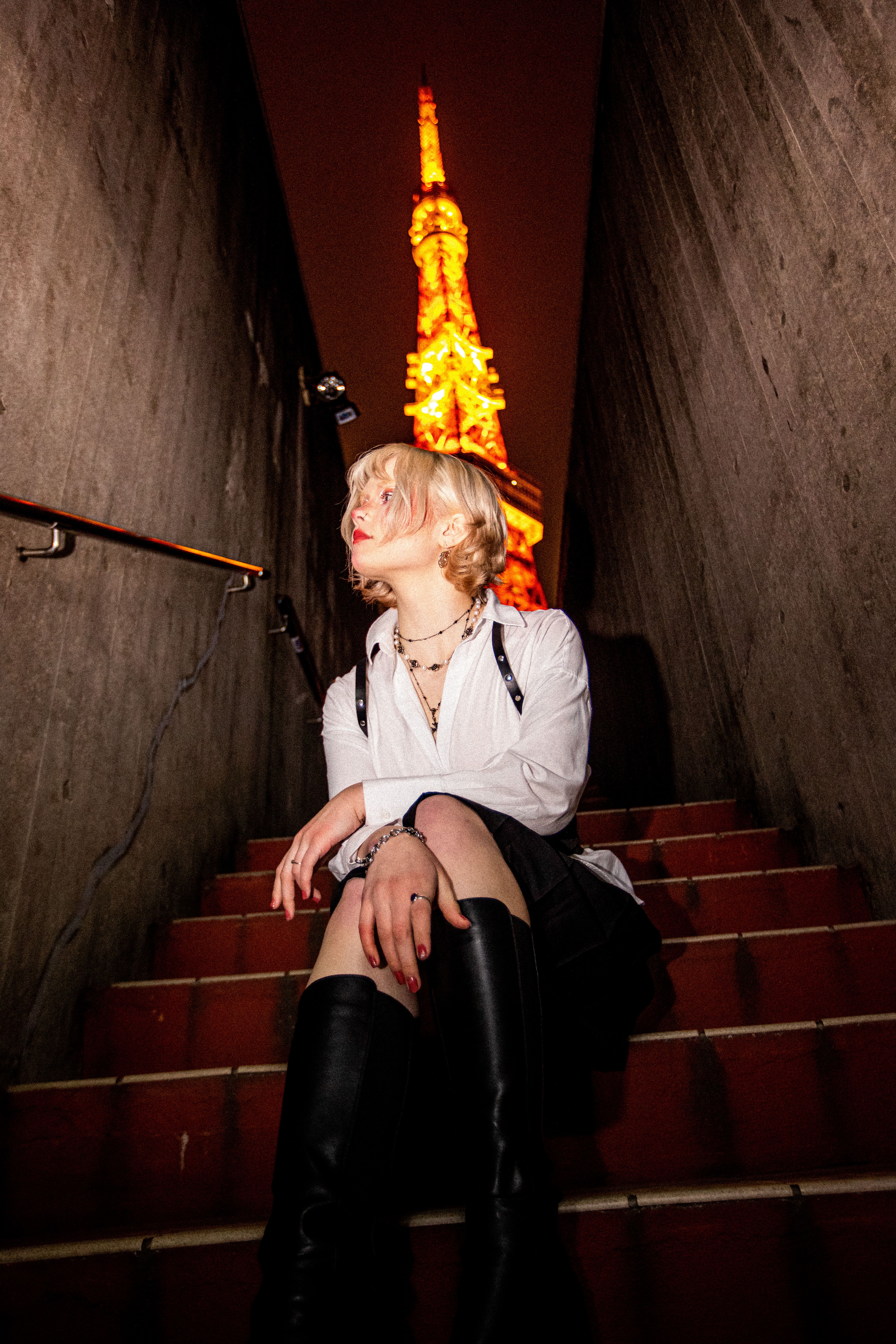 Fashionable woman seated at night with a towering structure in the background, creating a striking urban scene.
