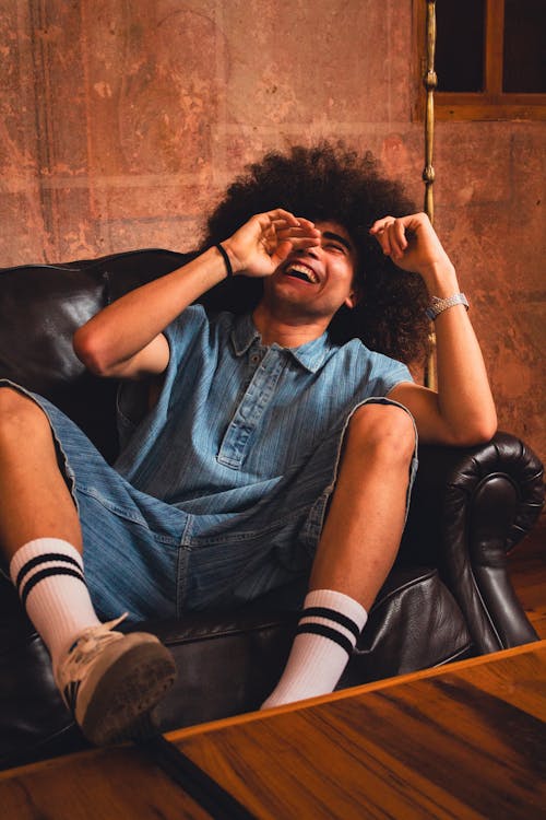 Free A Young Man in a Fashionable Outfit Sitting on a Sofa and Laughing  Stock Photo