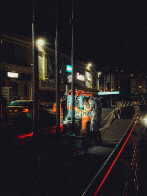Free A street vendor serves food at night in an urban setting, illuminated by city lights. Stock Photo