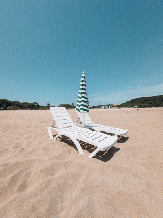 Two lounge chairs on a beach with an umbrella