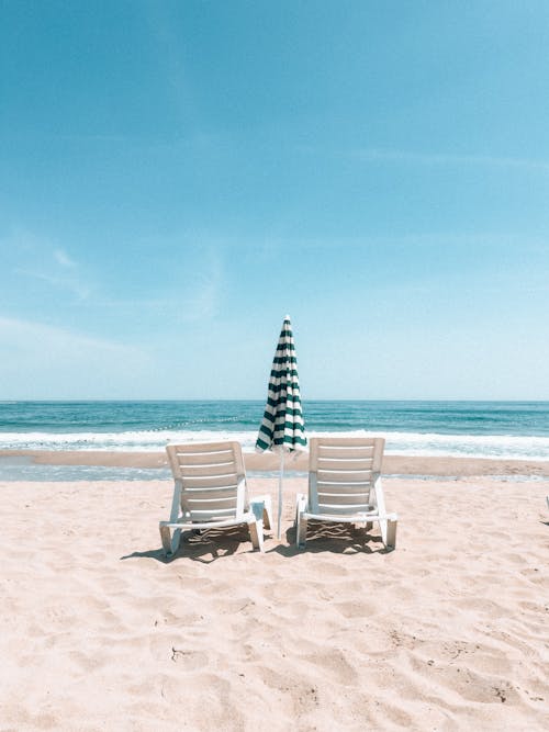 Two chairs on the beach with an umbrella