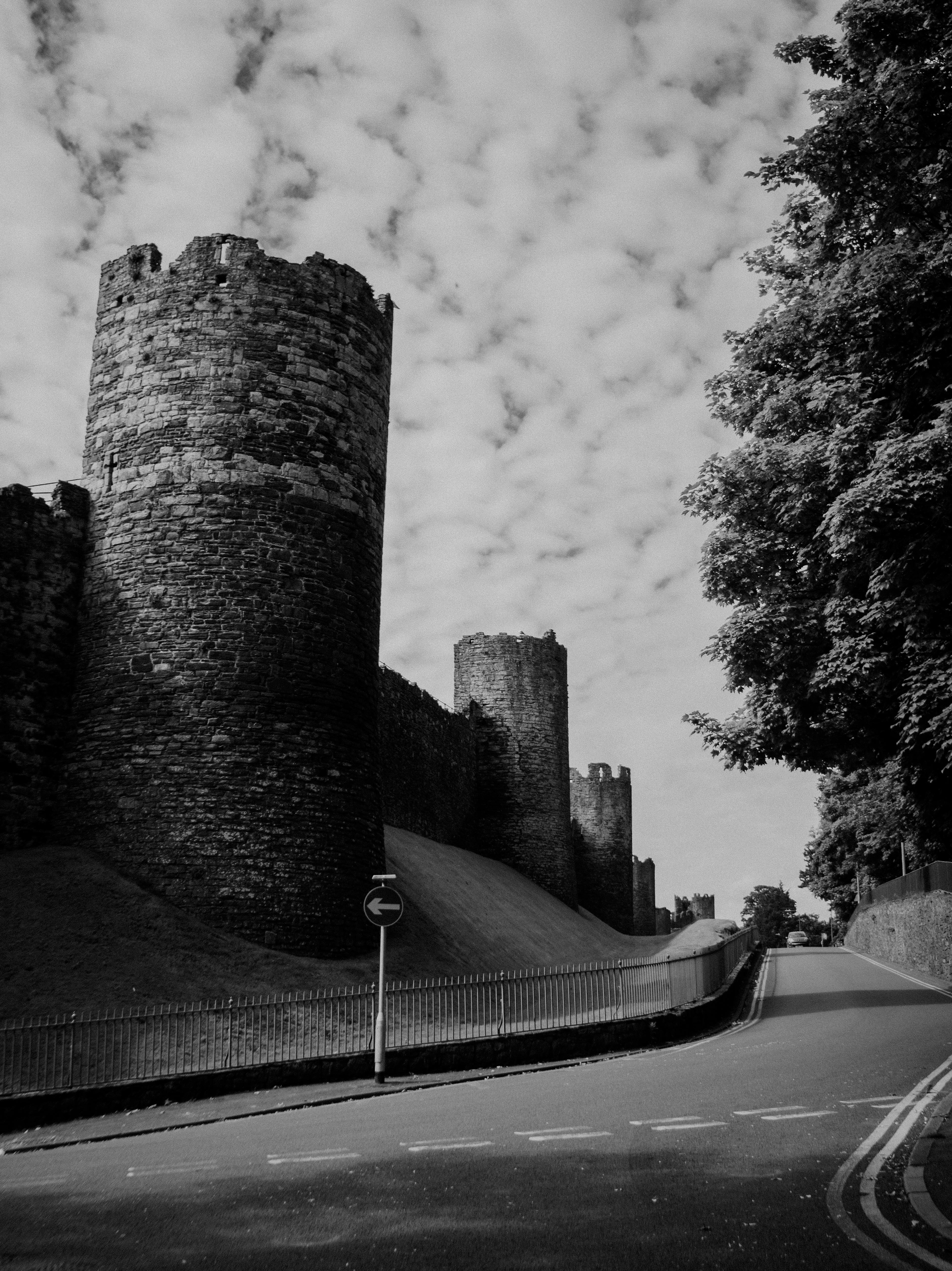 Dramatic black and white photo of Conwy Town Walls with road and trees.