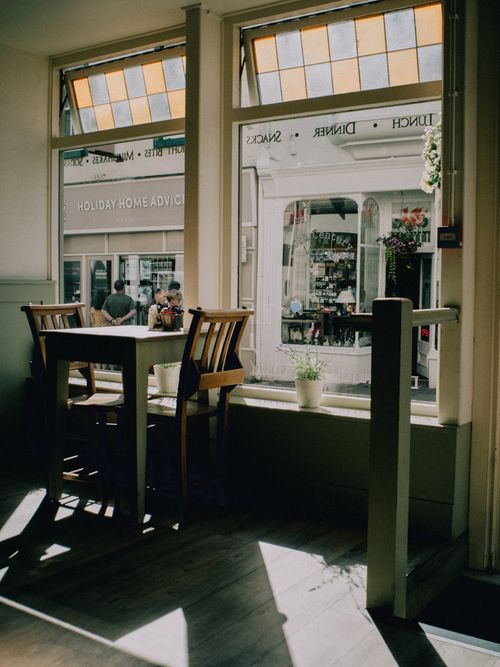 Free Warmly lit café interior in Conwy, Wales, featuring sunlit windows and empty tables. Stock Photo