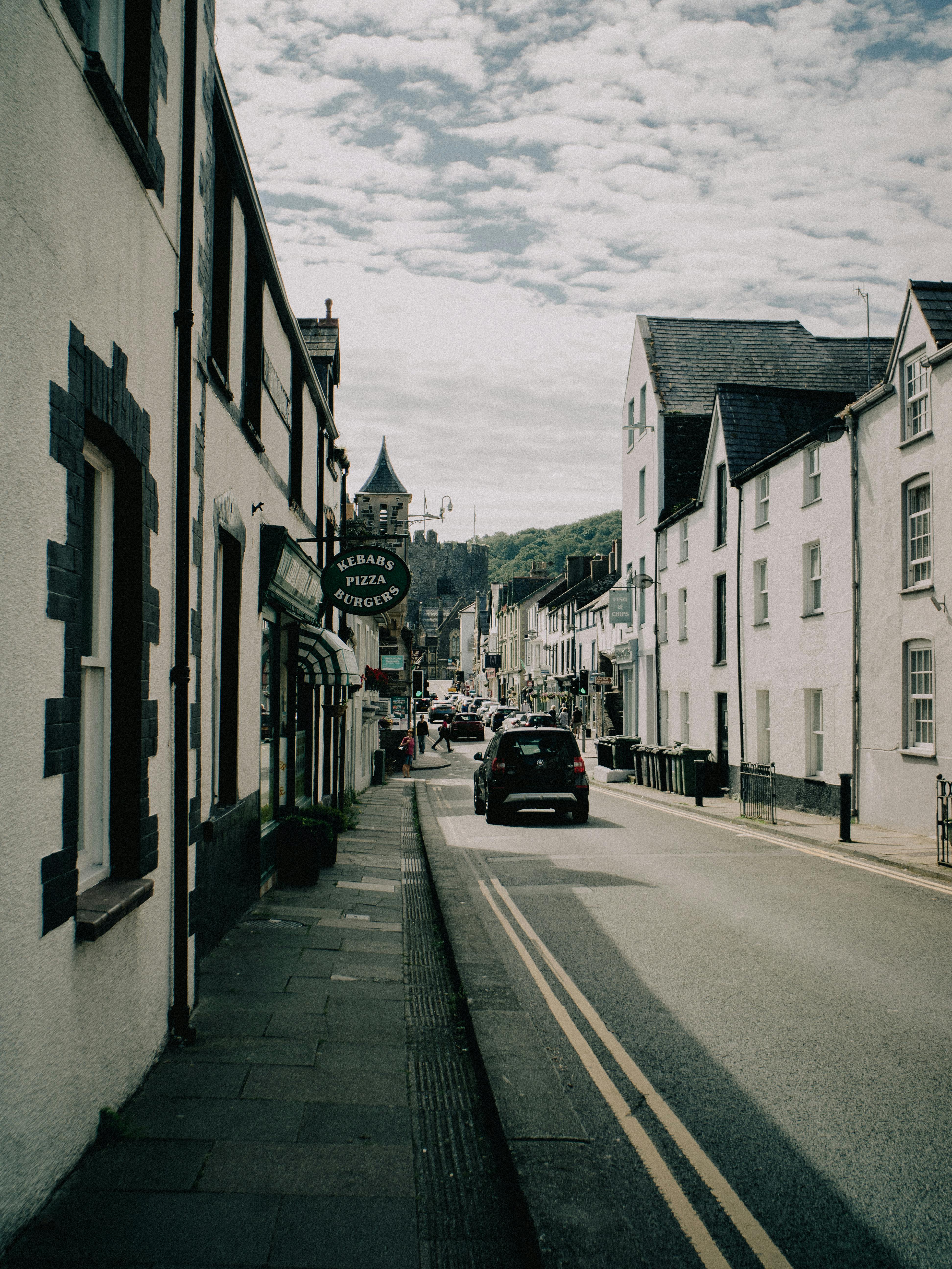 Picturesque view of a street in Conwy, Wales with historic buildings lining the roadway under a cloudy sky.