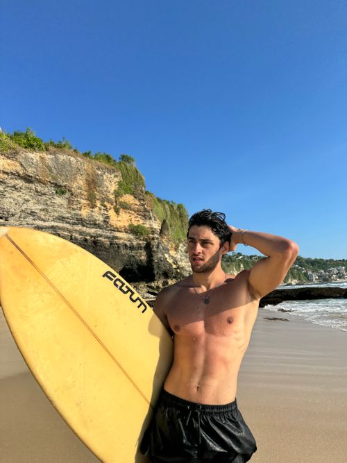 Free Shirtless man with a surfboard on a beach, enjoying a sunny day by the sea. Stock Photo
