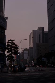 A moody urban scene at dawn showcasing city streets, cars, and tall buildings.