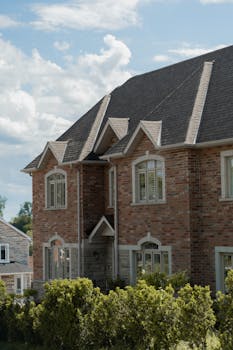 Charming brick house with gable roof surrounded by lush greenery under a clear blue sky.