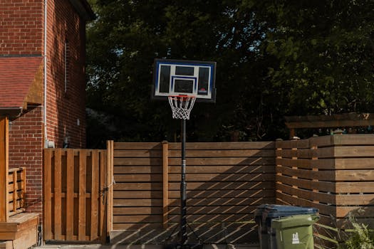 A backyard basketball hoop stands beside a brick house and wooden fence, ideal for outdoor sports.