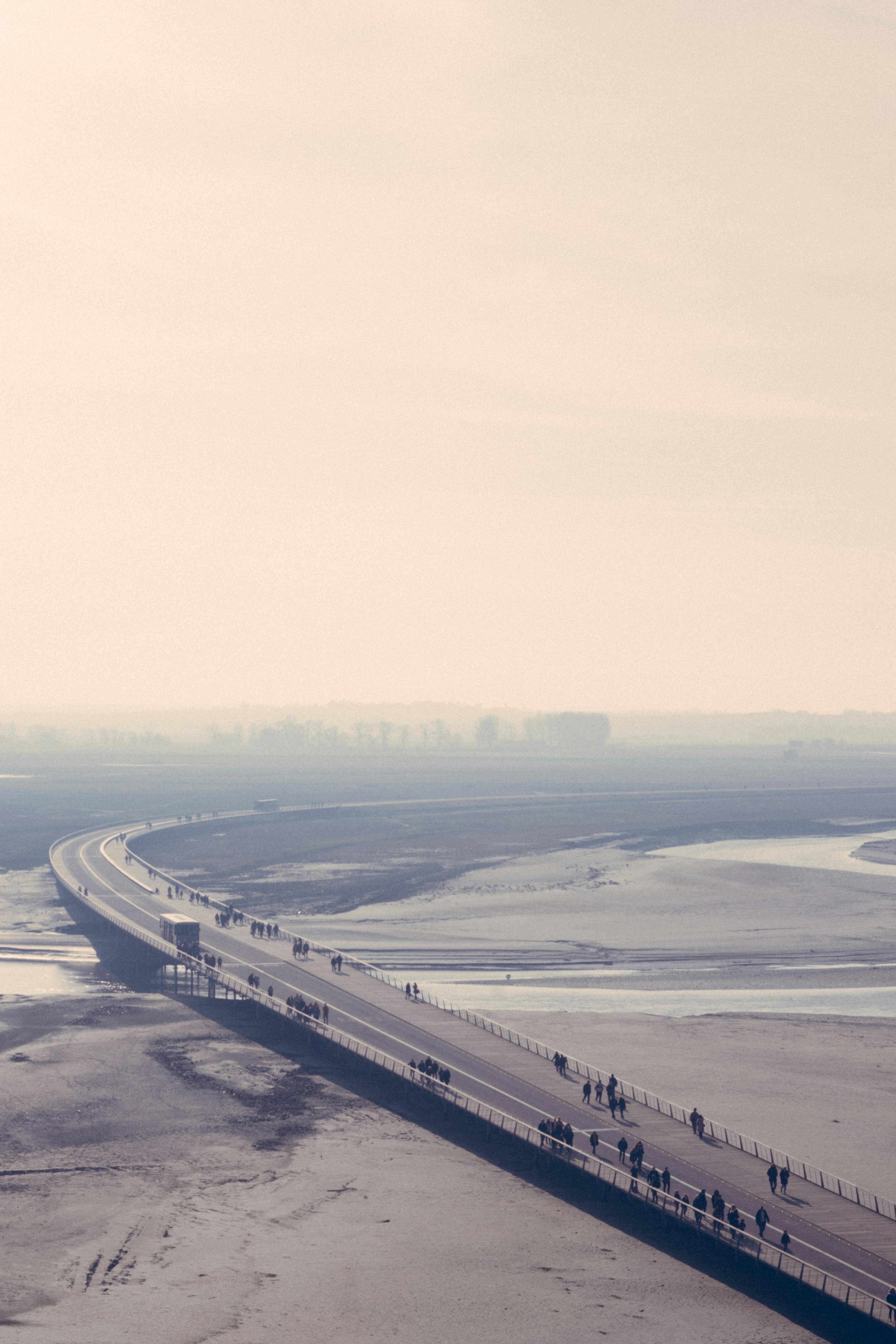 这张航拍照片捕捉了日落时分，人们沿着长桥在宁静水域上行走的静谧景象