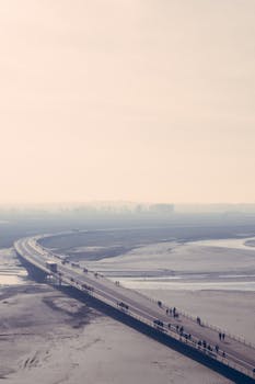 这张航拍照片捕捉了日落时分，人们沿着长桥在宁静水域上行走的静谧景象