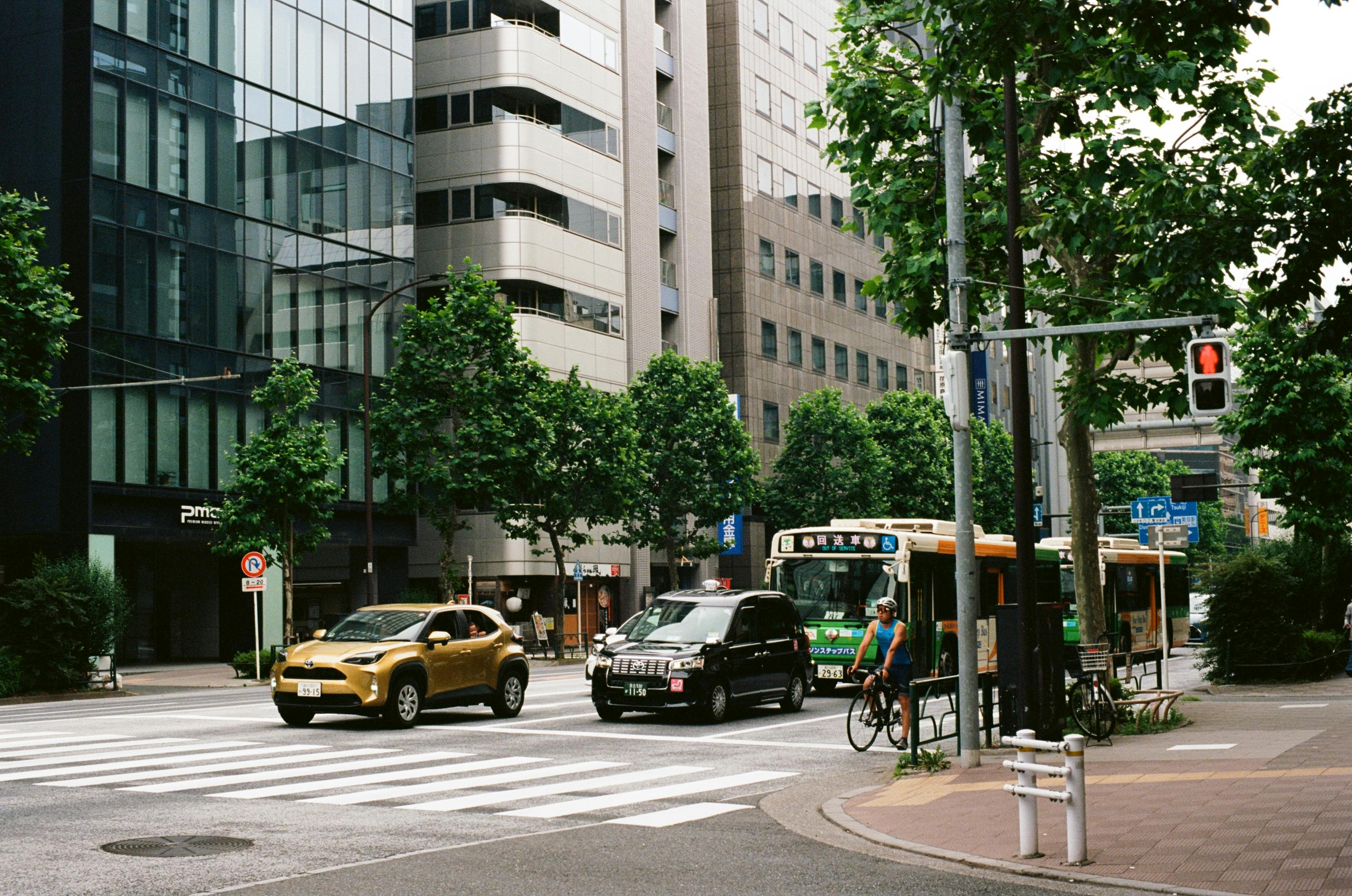A bustling Tokyo street with cars, a bus, and a bicyclist on a warm day.