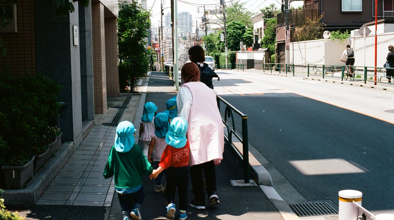 保育士が園児たちと手をつないで地域の街をお散歩している様子