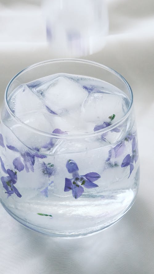 A glass of water with purple flowers in it
