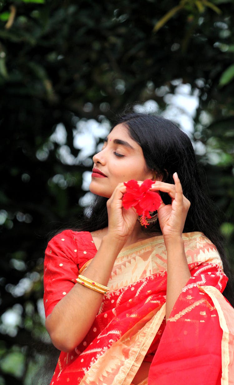 Woman In Red Sari Placing Flower In Her Ear