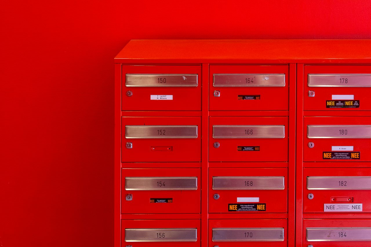 A row of sleek red mailboxes with metallic number panels and keyholes against a red background.