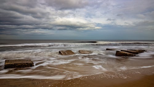 A beach with rocks and waves under a cloudy sky